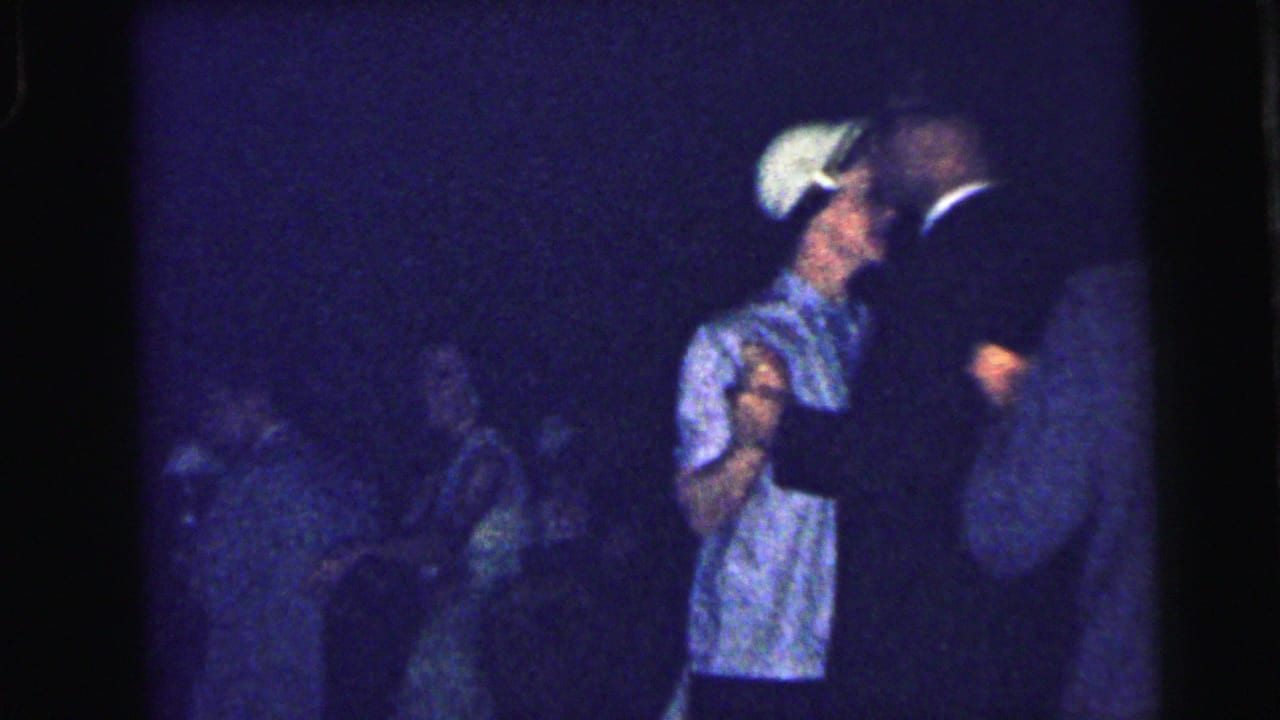 Couple dancing in a dim room while other guests sit or stand nearby.