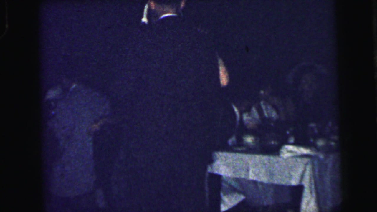 A dimly lit Camden social-event frame shows guests near a white-clothed table in 1964 home-movie footage.
