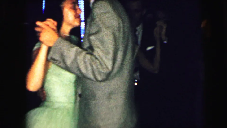 1964 Camden dance scene with a suited man and woman in a pale green dress holding hands beneath dim neon-like lights.