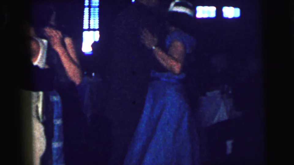 1964 Camden frame showing couples dancing in a dim venue, with a blue-dressed woman and suited dancers under vertical blue lights.