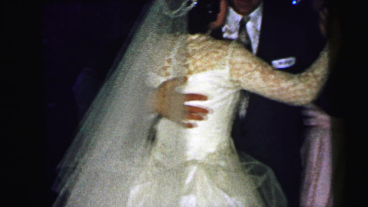 Bride in a lace dress and veil dances closely with a groom in a dark suit.