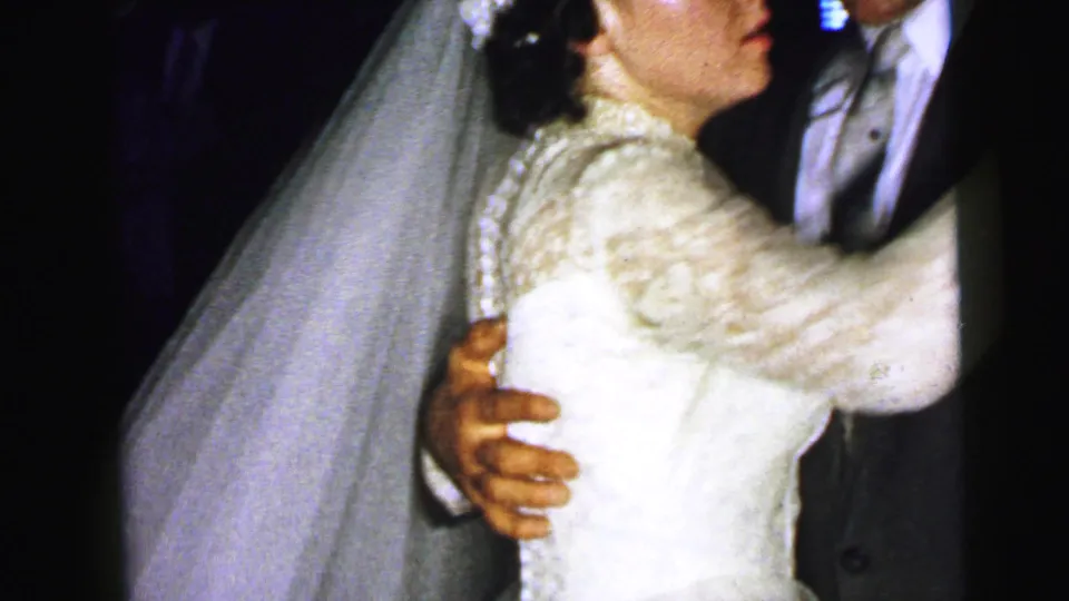Close handheld 8mm view of the bride's lace bodice, veil, and the groom's arm during the 1964 wedding dance.