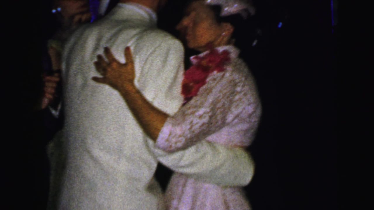 A woman wearing a lace dress, small hat, and red floral accent dances with a man in a light suit at the Camden formal event.