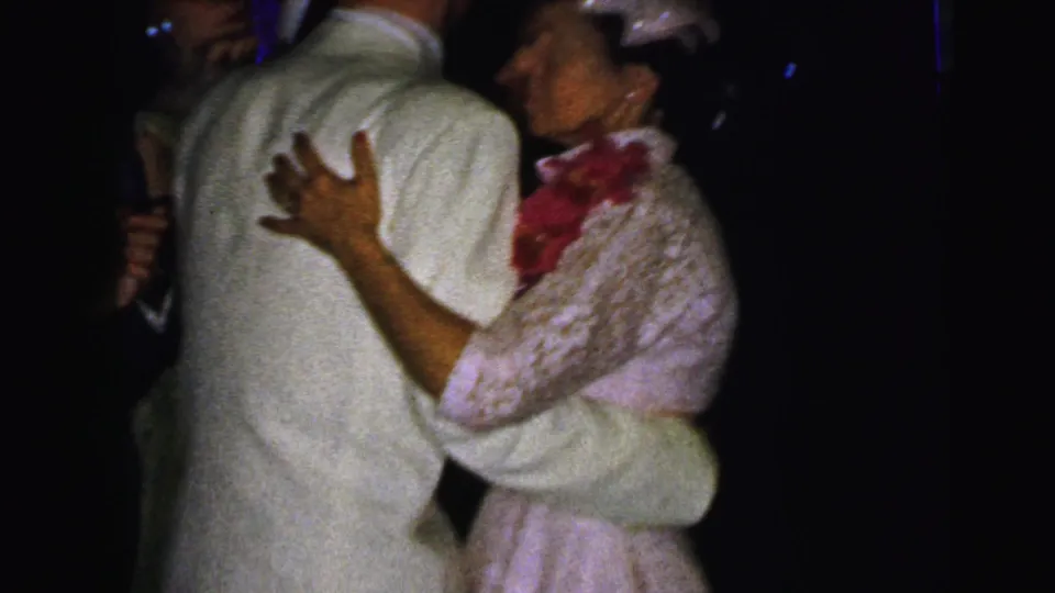 A woman wearing a lace dress, small hat, and red floral accent dances with a man in a light suit at the Camden formal event.