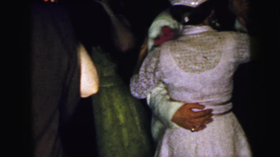 The dancing couple is seen from behind and partly obscured, with the woman's white lace dress and the man's arm around her waist visible.