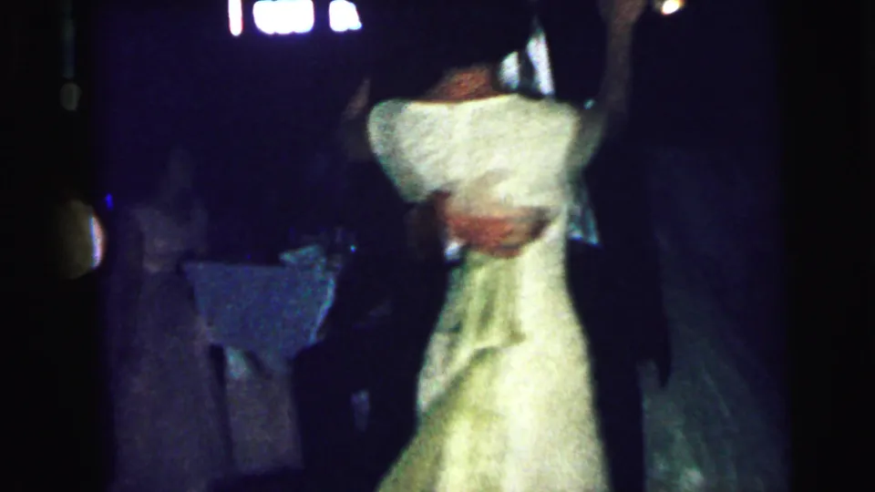 A couple dances from behind at the 1964 Camden wedding reception, with the woman's light dress standing out in the dark room.