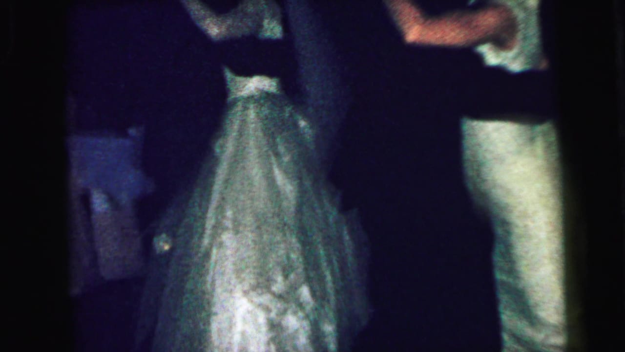Couples in formal clothing dance closely in a dim room.