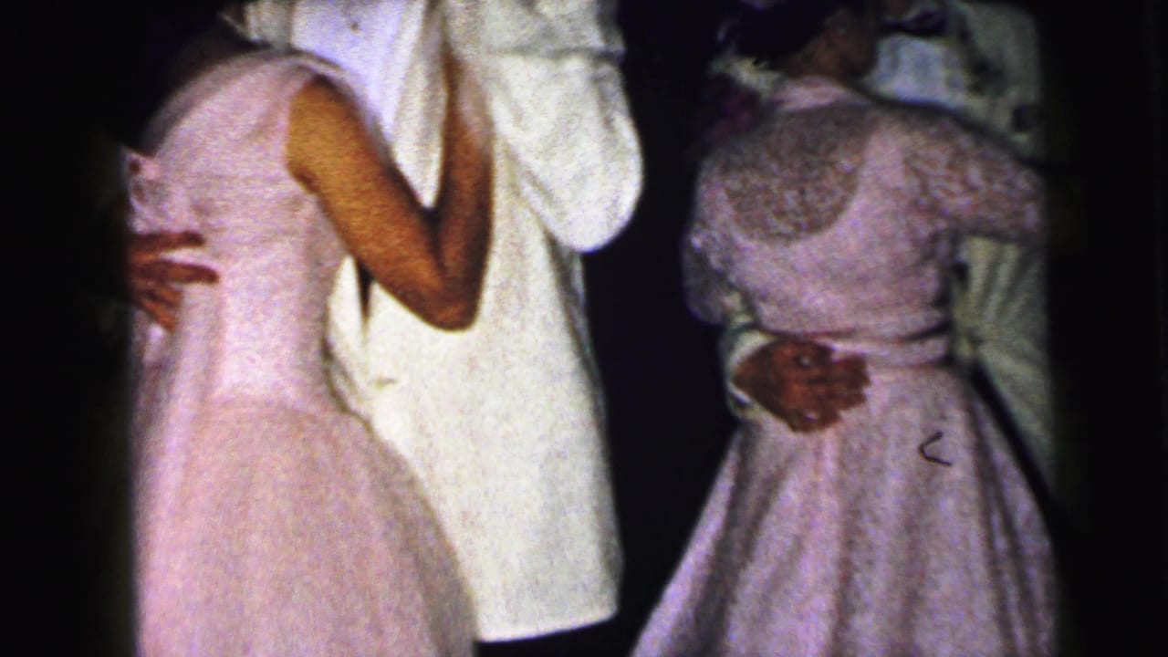 A young woman in a pale full-skirted dress dances closely with a partner in a white jacket in the Camden 1964 home-movie clip.
