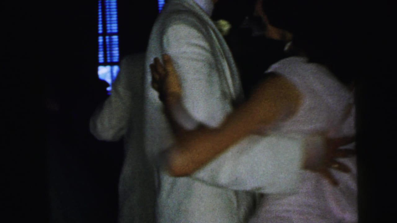Couple dancing closely in a dim room, with the woman's hand on the man's back.