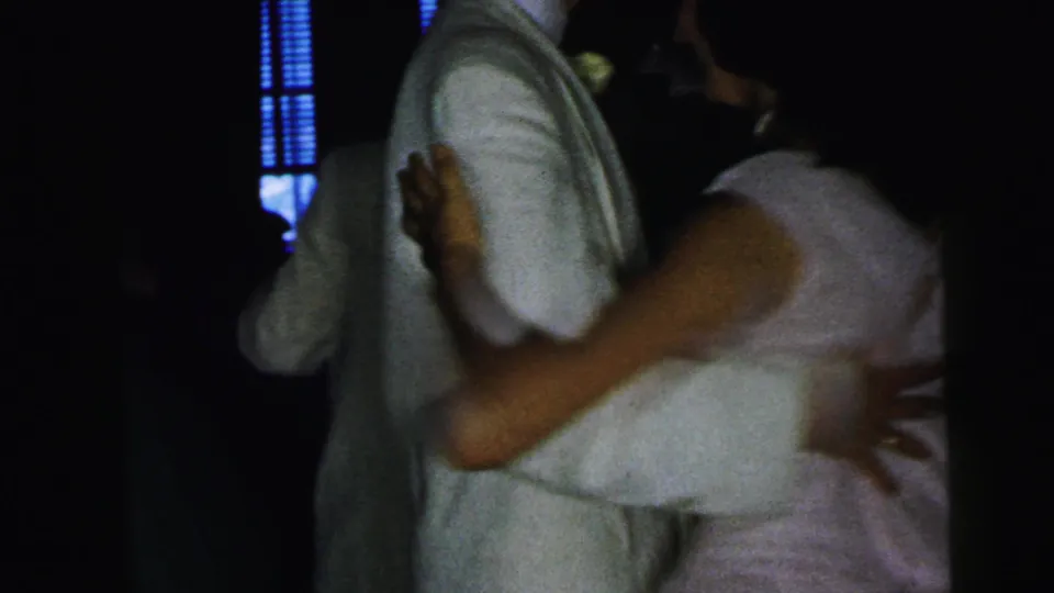 In 1964 Camden home-movie footage, a couple dances closely in low light while a blue window-like glow appears behind them.