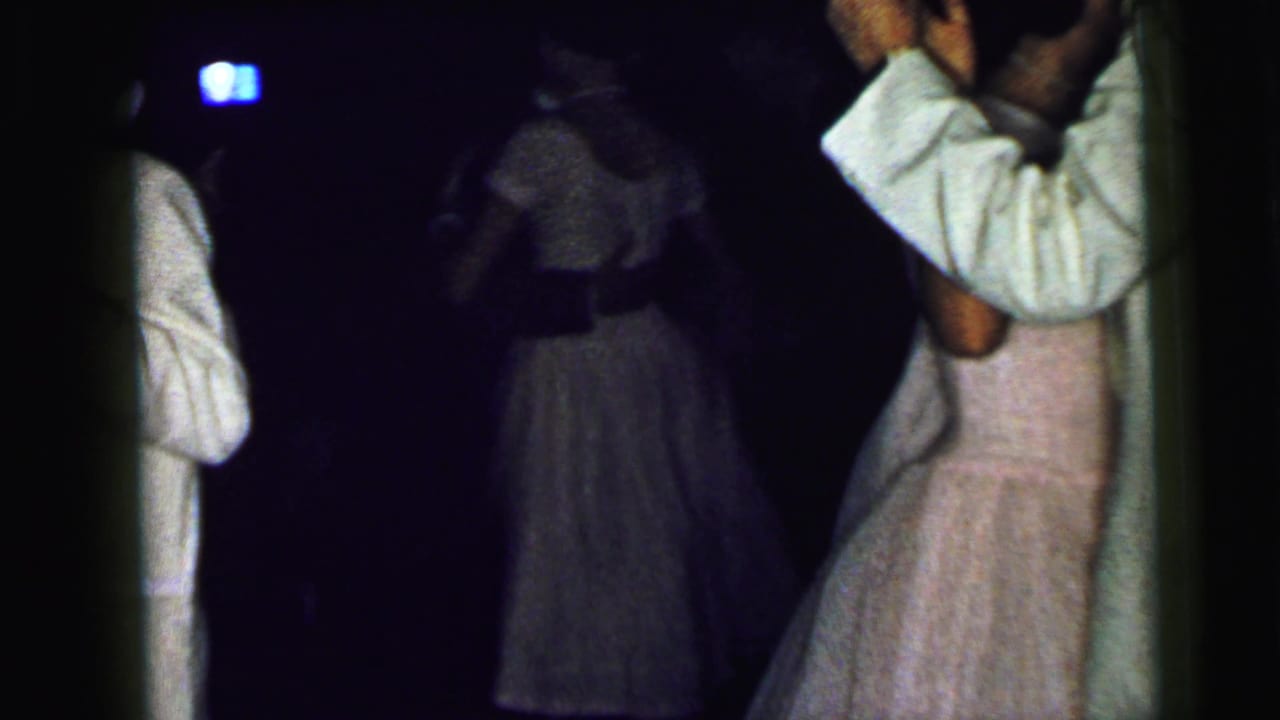 1964 Camden wedding home movie frame showing couples dancing in low light, with a man in a white suit near a woman in a pale pink dress.