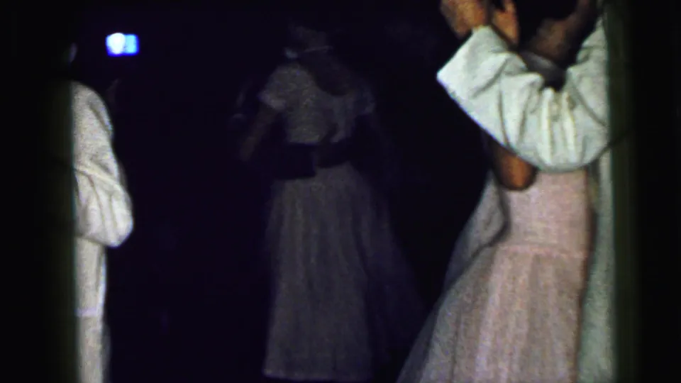 1964 Camden wedding home movie frame showing couples dancing in low light, with a man in a white suit near a woman in a pale pink dress.