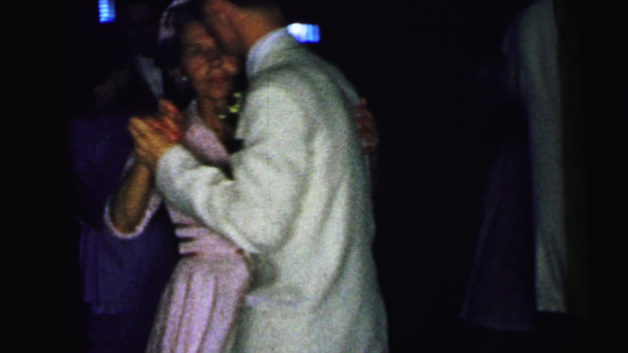 A groom in a white suit appears to dance with an older woman in a light pink dress during a 1964 Camden wedding reception.