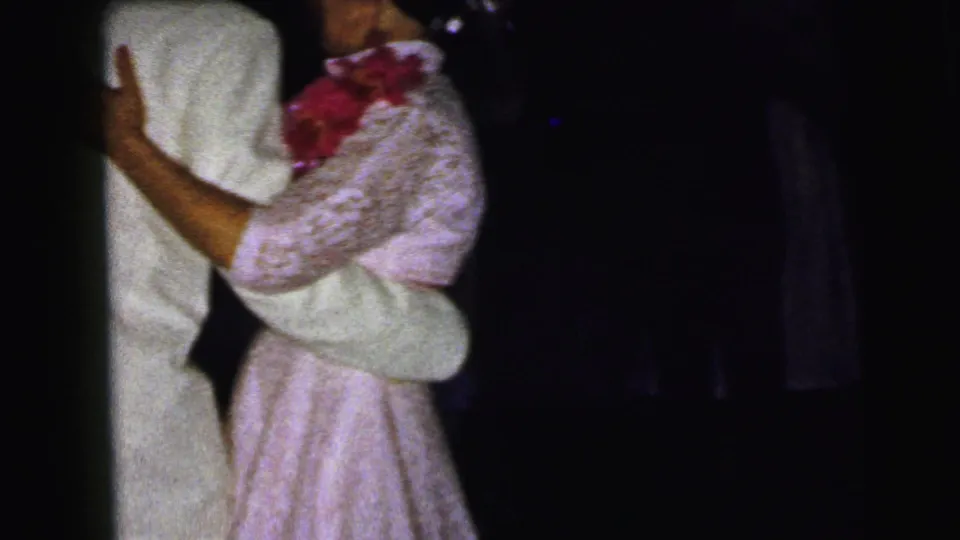 1964 Camden wedding frame showing a woman in a pink lace dress dancing with a man in a white suit, with other guests faintly visible.