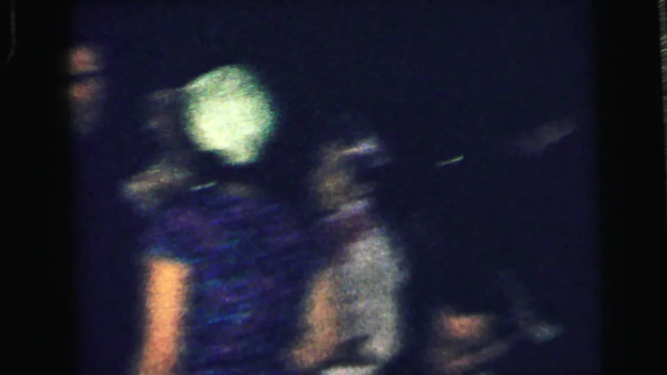 Motion blur and low exposure obscure the 1964 Camden party scene as adults shift position, with a pale hat and patterned dress visible.