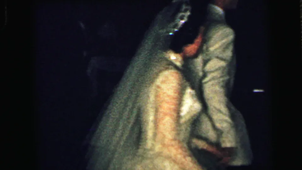 1964 Camden home-movie frame showing the bride and groom walking arm-in-arm during their wedding reception.