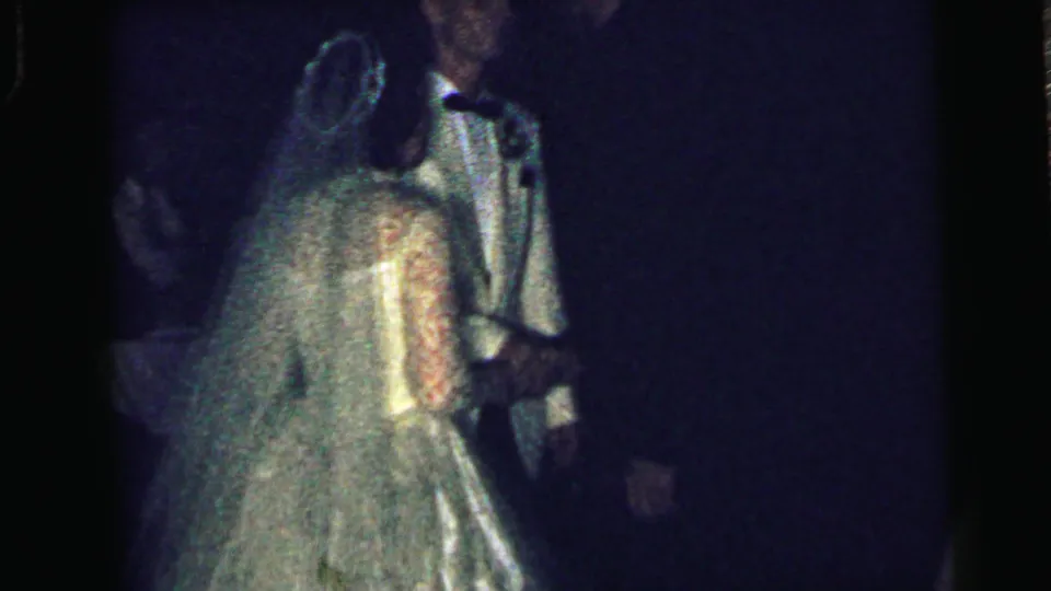 1964 Camden wedding footage showing the bride from behind in her veil as she faces the groom in a dim reception room.
