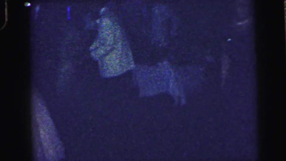 Blue-tinted 8mm frame from the Camden reunion dance with a faint adult figure moving in the dim room.