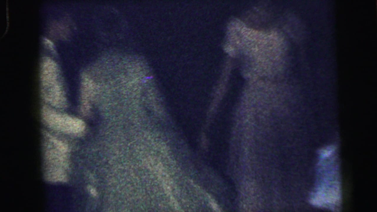 Dim, grainy view of party guests near a dancer in a green dress.