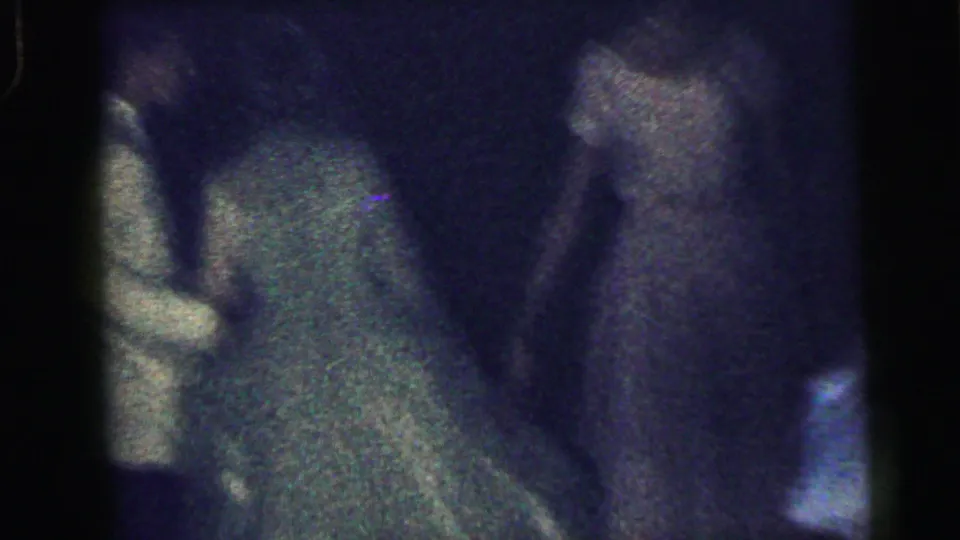 Grainy 1964 Camden home-movie frame showing guests around a dancer in a green formal dress in low light.
