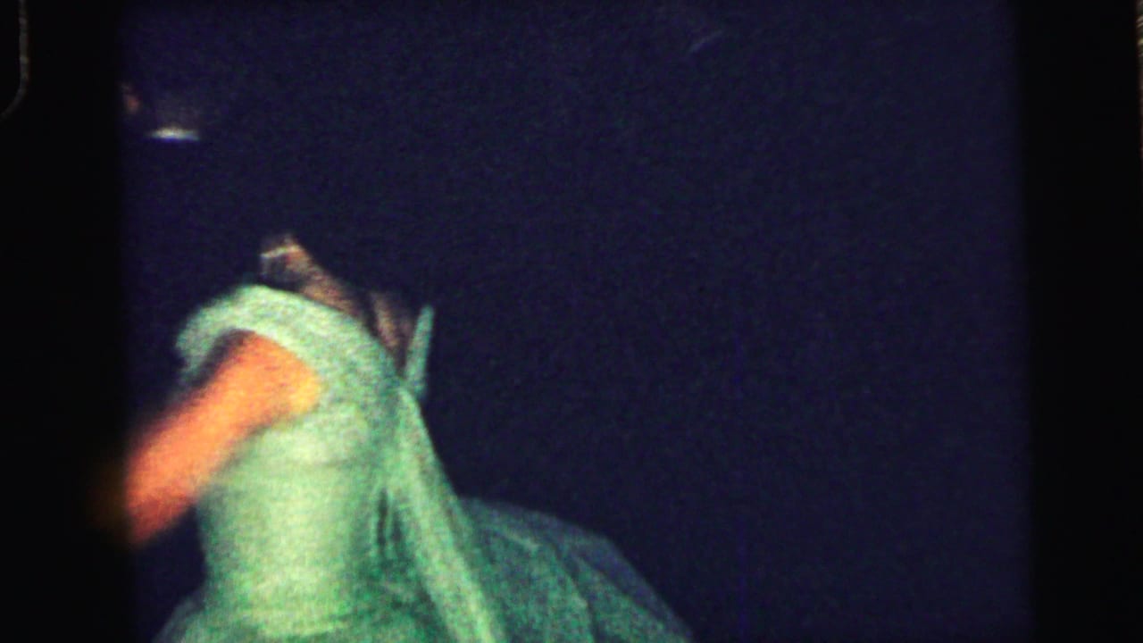 Woman in a green formal dress turns while dancing in a dark room.