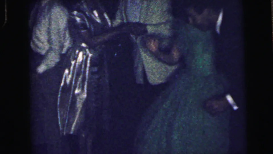 Dim 8mm frame of the formal party with suited guests and a woman in a green dress near the edge of the group.