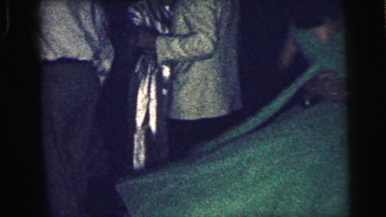 Dim party room with people standing and a green-shirted figure partly visible near the lower frame.