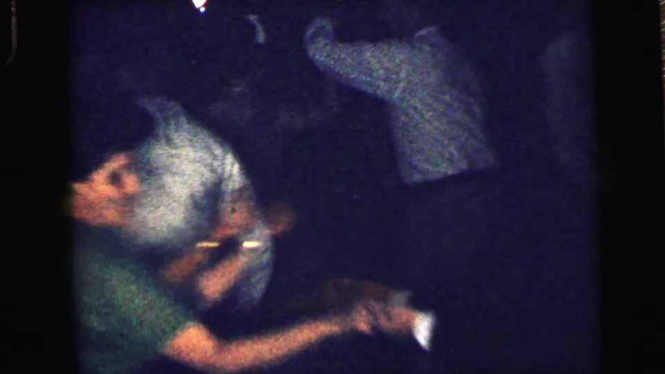 Two adults appear close together during the 1964 Camden party scene, with other figures blurred in the background.