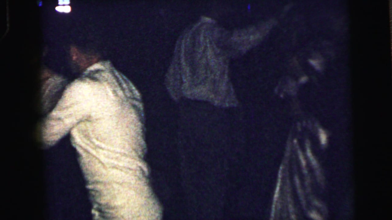 1964 Camden home-movie frame of formally dressed adults dancing closely, with other party guests partly visible in the dark background.