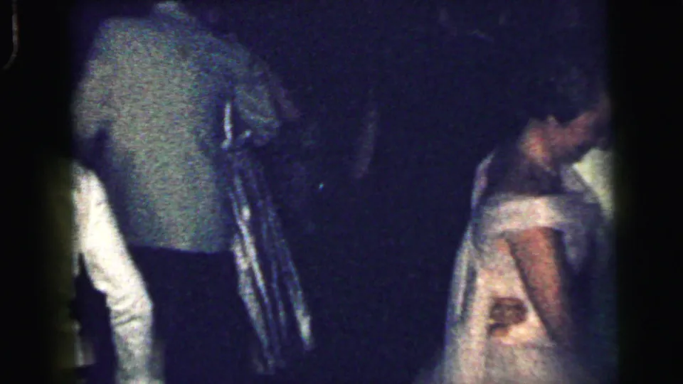 1964 Camden home-movie frame with adults in formal wear dancing closely in a dark room, captured with visible 8mm grain and blur.
