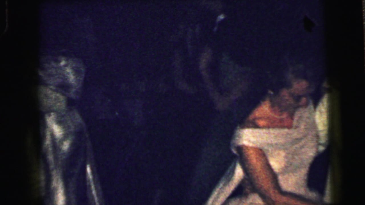 Woman in a white gown seated or leaning during a dim formal dance scene.