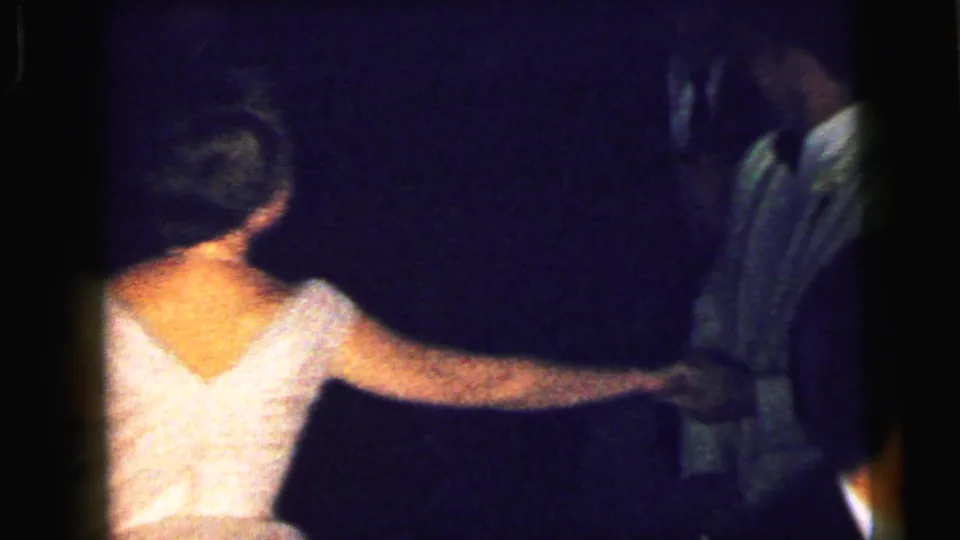1964 Camden formal-party frame showing a woman in a white gown holding hands with a tuxedoed dance partner.
