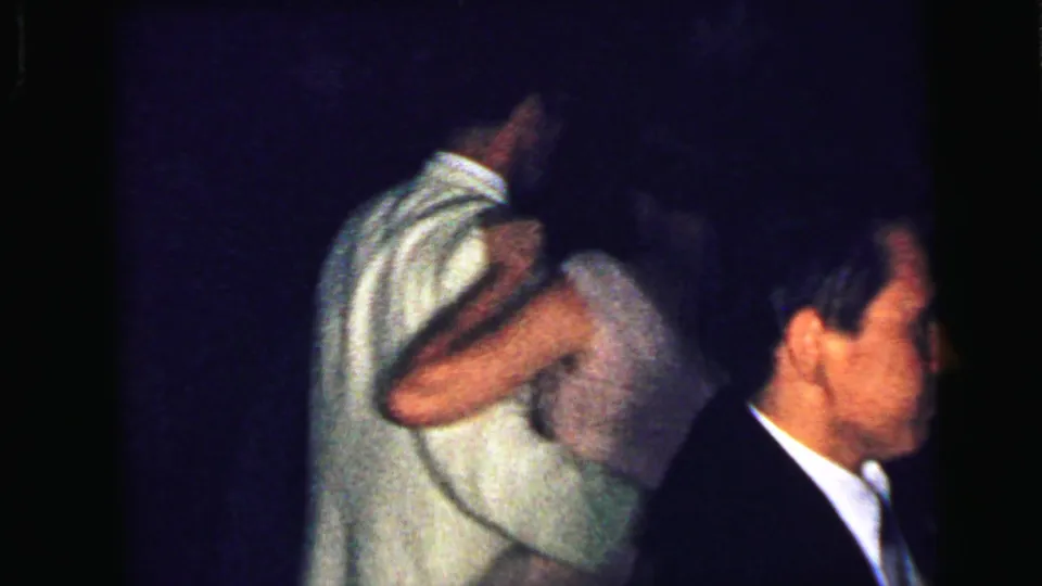 A couple dances closely in the dim Camden 1964 room, partly blocked by a man in a dark suit in the foreground.