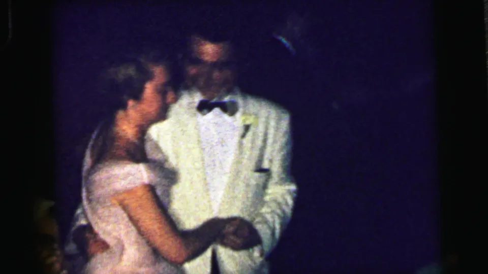 A woman in a pale pink dress dances with a man in a white dinner jacket and black bow tie in Camden 1964 home-movie footage.