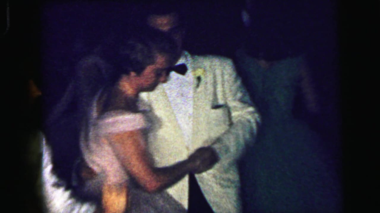 In 1964 Camden home-movie footage, a man in a white dinner jacket dances closely with a woman in a light gown under dim lighting.