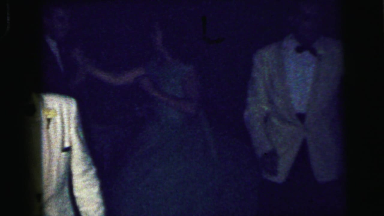 A low-light 8mm frame shows formal-dressed guests on the dance floor, with a white tuxedo jacket partly visible near the center.