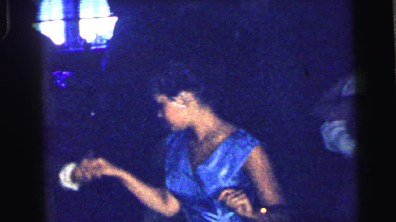 Woman in a bright blue sleeveless dress dancing in a dark room.