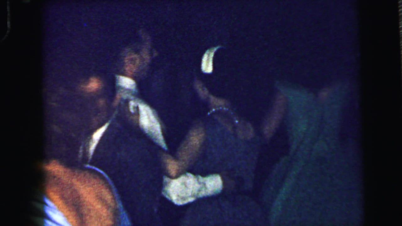 Adults in formal clothing dance in dim blue lighting.