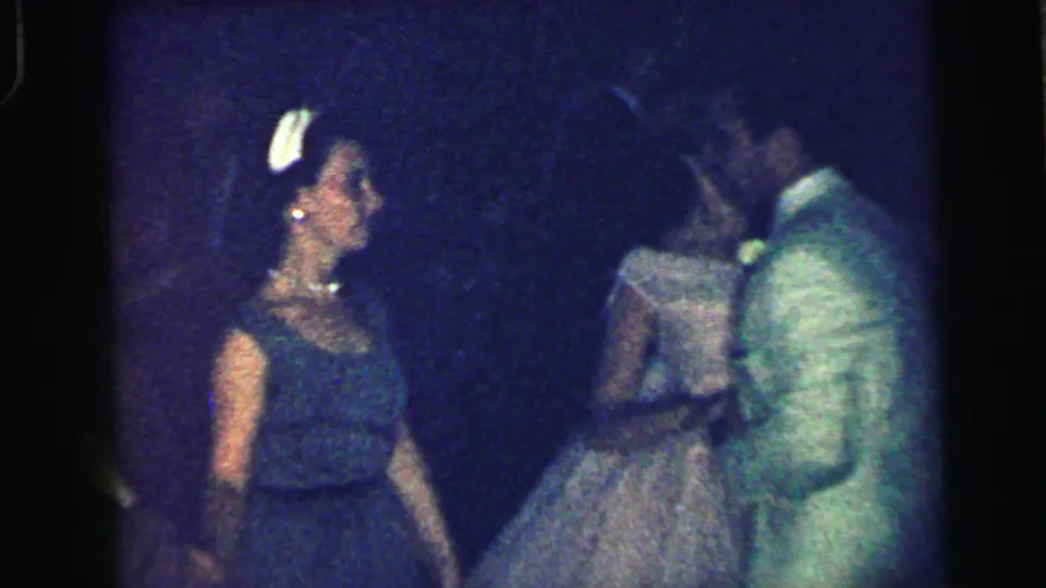 A woman in a dark formal dress stands near a man in a light suit during the 1964 gala footage.