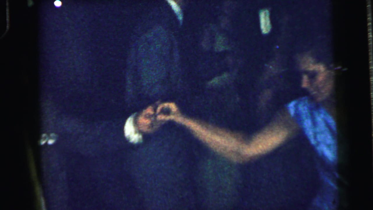Woman in a blue dress dances with another guest in a dim party room.