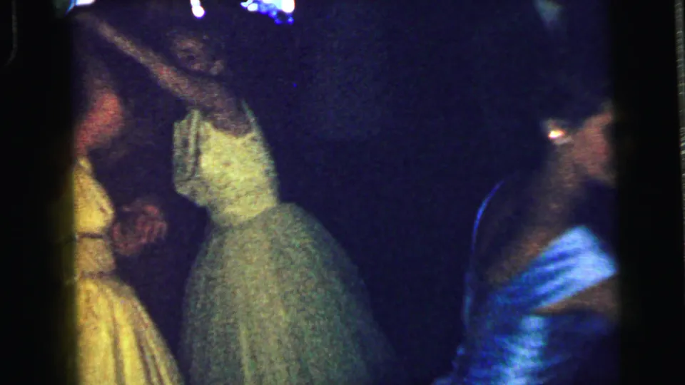 Women in yellow, pale green, and blue dresses dance at the Camden formal party, with a suited man visible in the background.