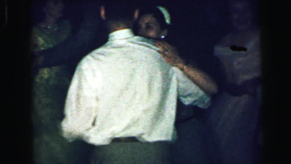 1964 Camden home-movie frame showing a man in a white shirt dancing closely with a woman in a dark sleeveless dress.