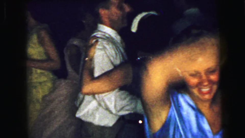 1964 Camden home-movie frame with adults dancing indoors and a smiling woman partly cut off near the right edge of the frame.
