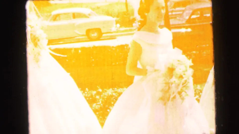 An overexposed 8mm frame shows brides with bouquets outdoors in Camden, with a car and street detail behind them.
