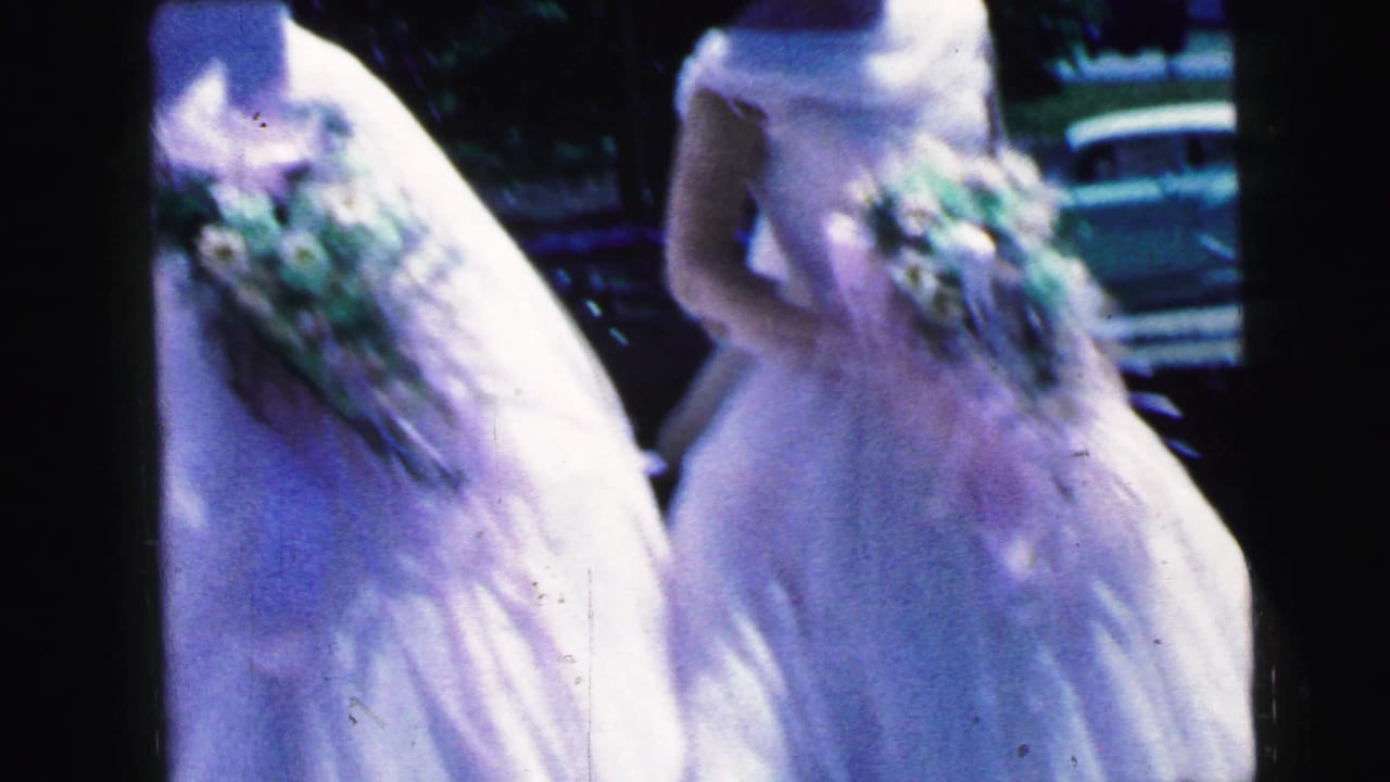 Close view of white formal dresses and bouquets with a parked car in the background.