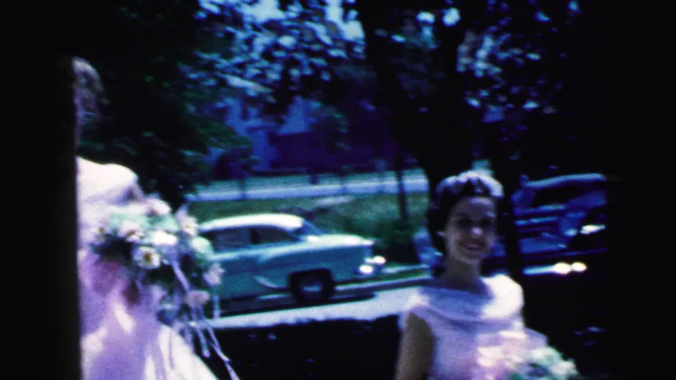 Camden, New Jersey 1964 frame with smiling young women in white formal dresses and bouquets, seen beside trees and parked cars.
