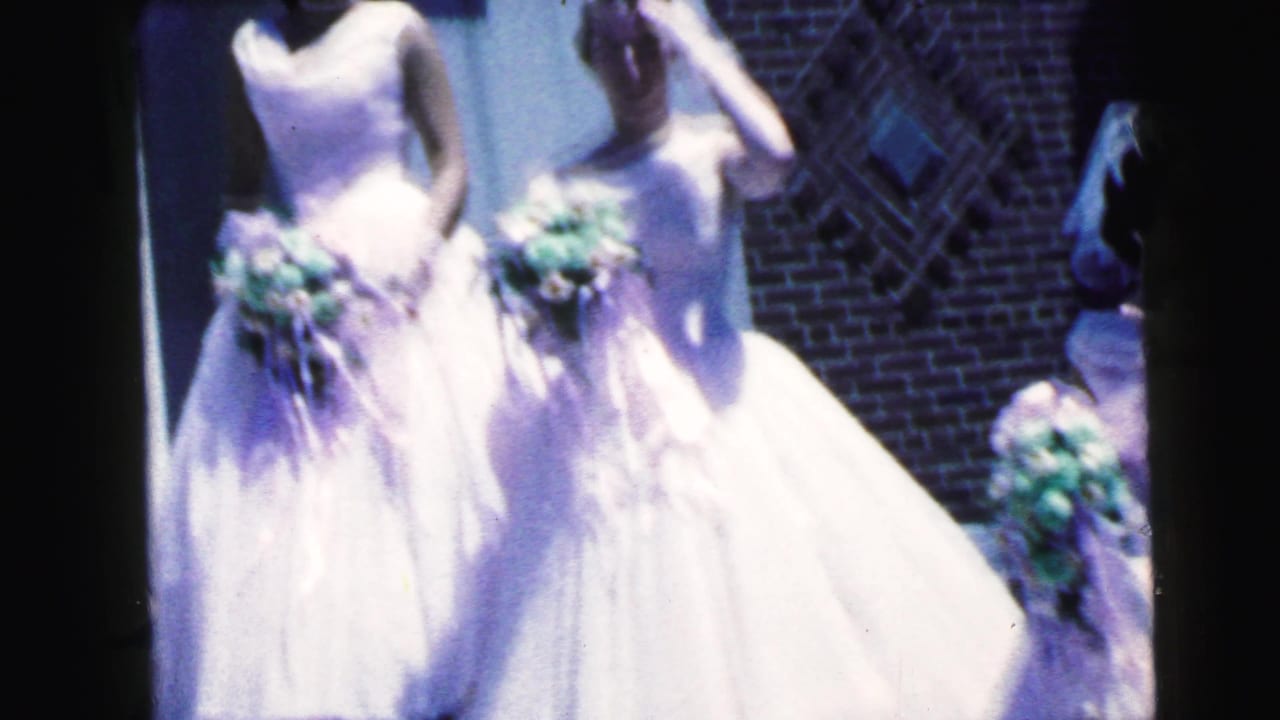 Cropped 1964 home-movie frame of bridesmaids in white gowns holding bouquets outside the Camden church.