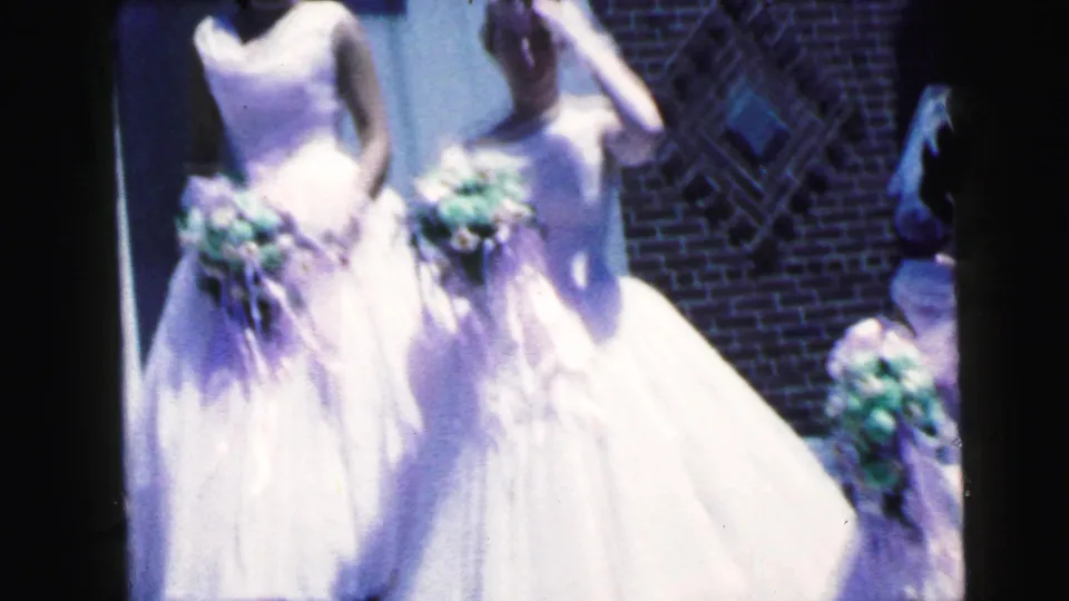 Cropped 1964 home-movie frame of bridesmaids in white gowns holding bouquets outside the Camden church.