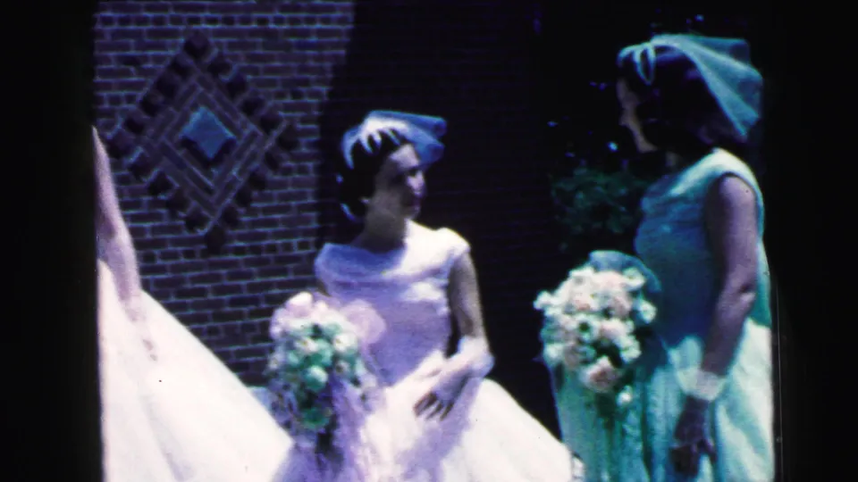 A bridesmaid in a white gown and headpiece stands beside a woman in mint formalwear outside the Camden church.