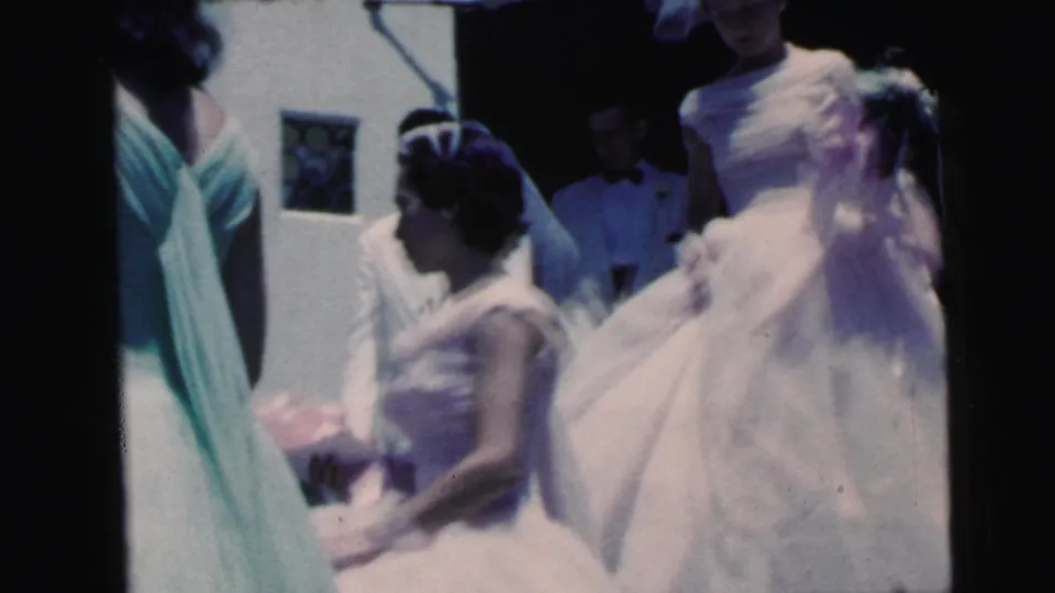 1964 Camden wedding frame with bridesmaids in voluminous pale dresses and veils standing beside the bride in green, with attendants partly visible behind.